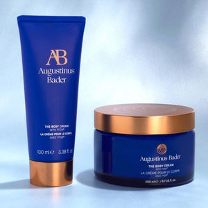 Two Augustinus Bader body cream products on a light gray background