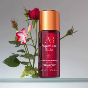 A bottle of the geranium rose body oil with red and white flowers behind it