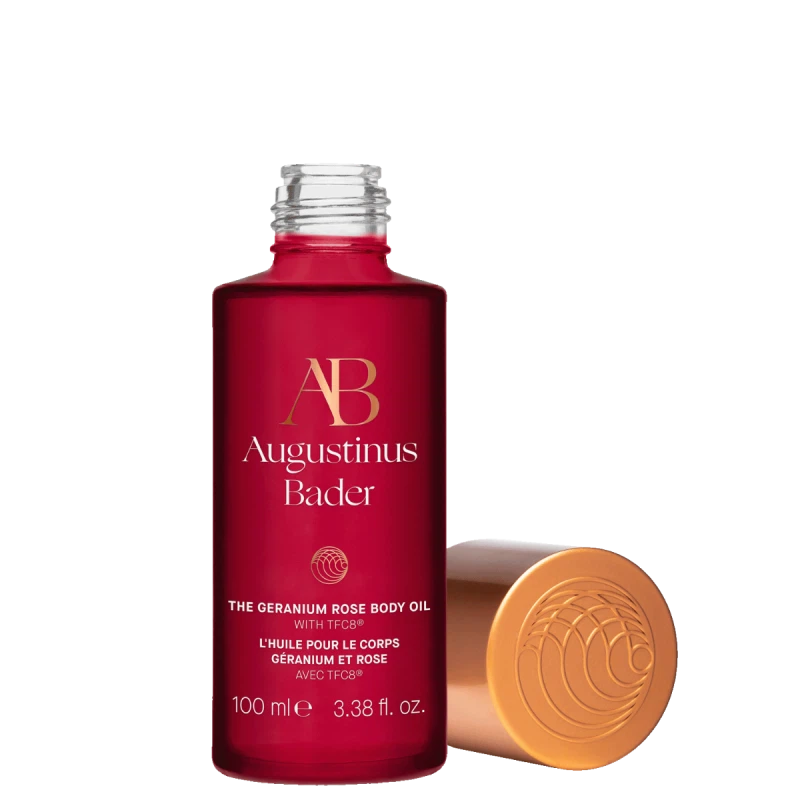 Red bottle of Augustinus Bader body oil with gold cap on a white background