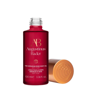 Red bottle of Augustinus Bader body oil with gold cap on a white background