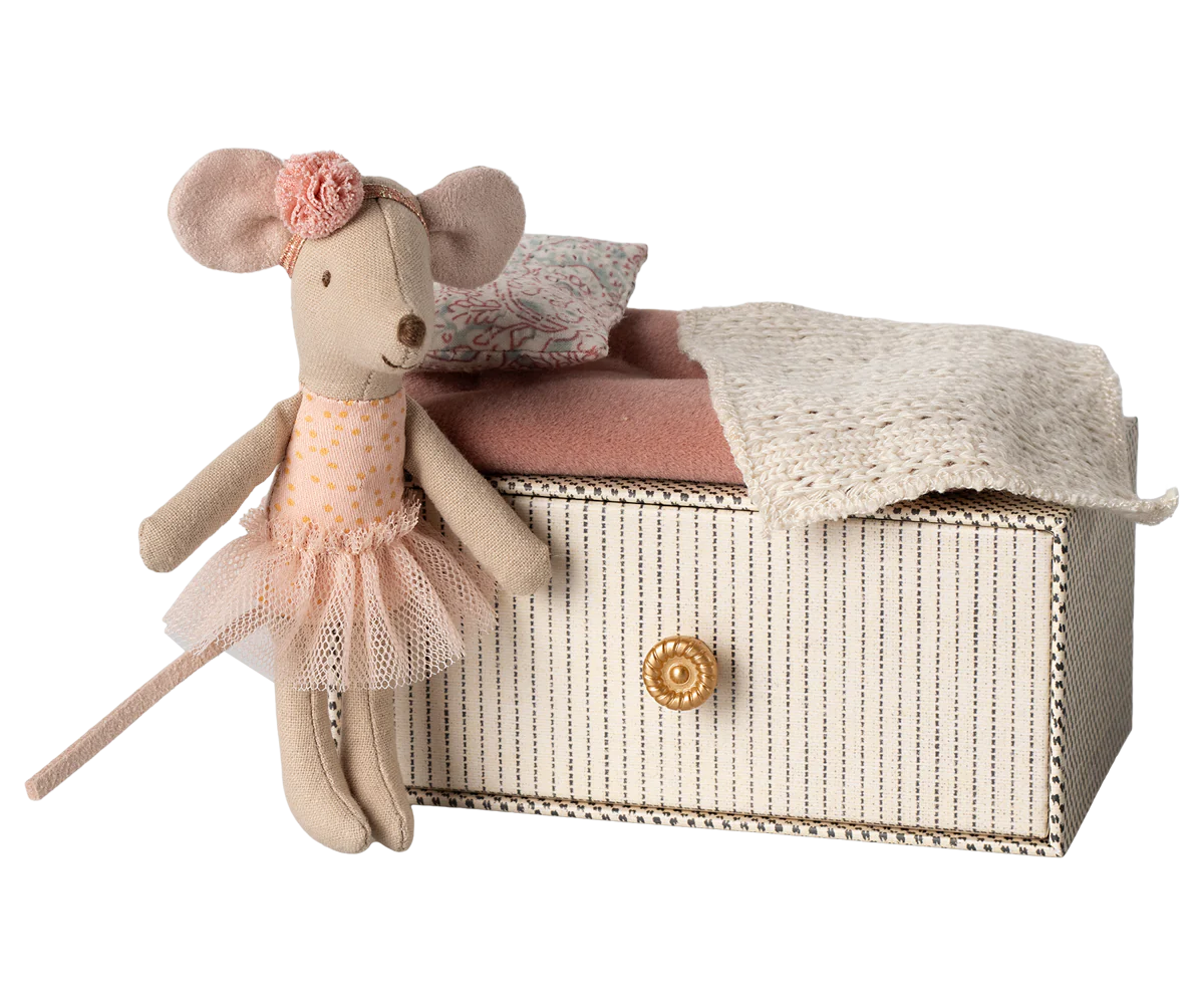 A toy mouse with a pink dress and flower decoration sitting on top of a daybed.