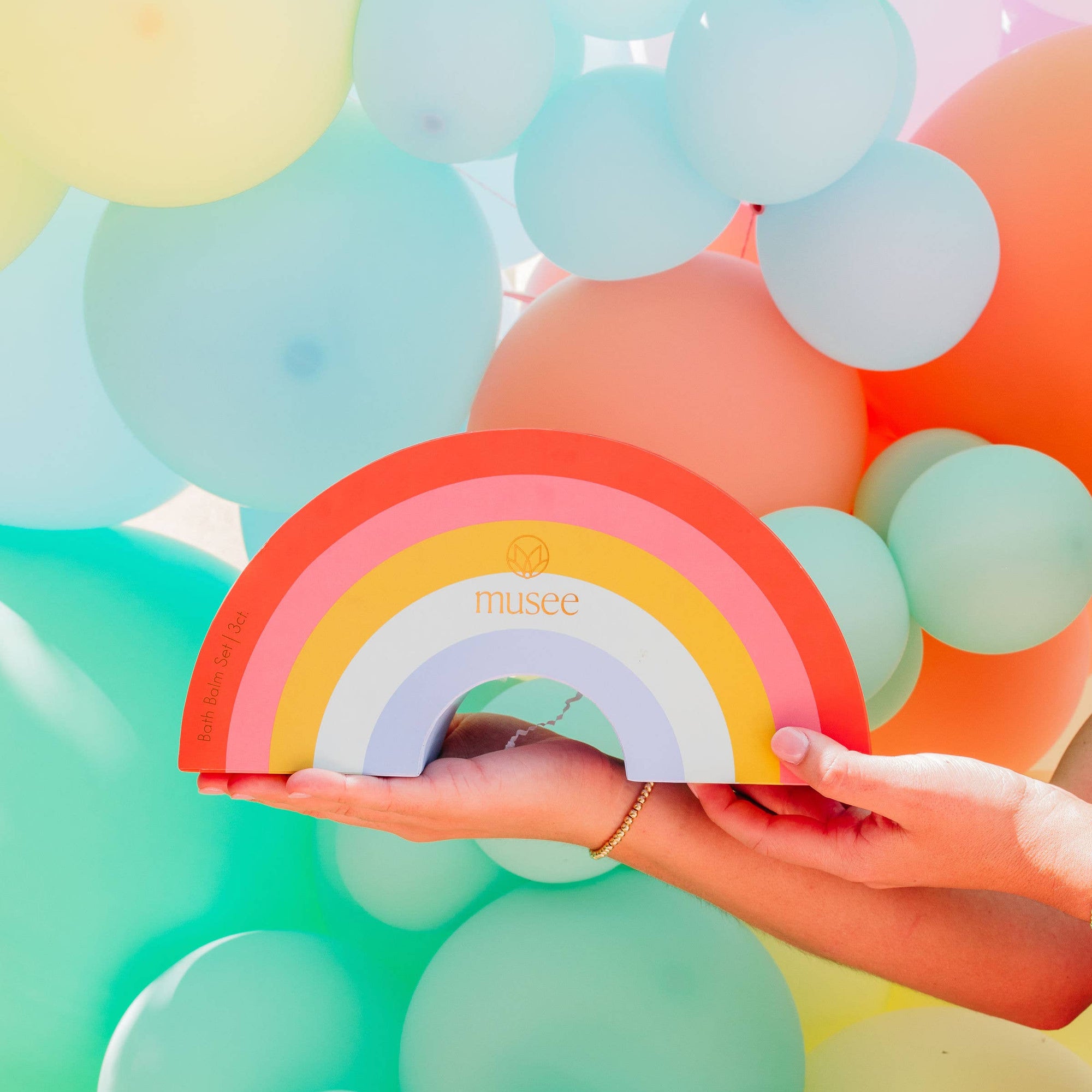Person holding a colorful rainbow-shaped object with balloons in the background