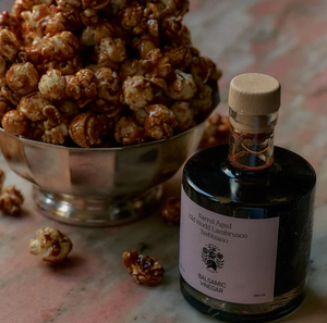 A bottle of Flamingo Estate barrel aged balsamic vinegar, next to a silver bowl full of popcorn