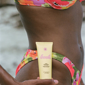 A person holding a tube of Bask sheer moisturizing sunscreen, SPF 50 lotion