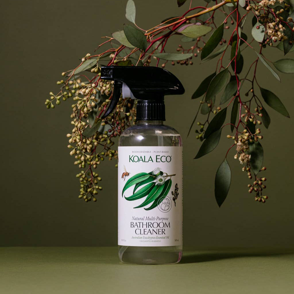 A bottle of koala eco bathroom cleaner and a flower on a green background. 