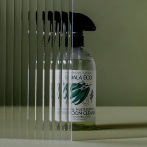 A bottle of koala eco bathroom cleaner and a flower on a green background. 