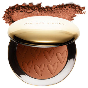 Compact powder with heart designs and 'Westman Atelier' branding, featuring a swatch of brown color on a white background.