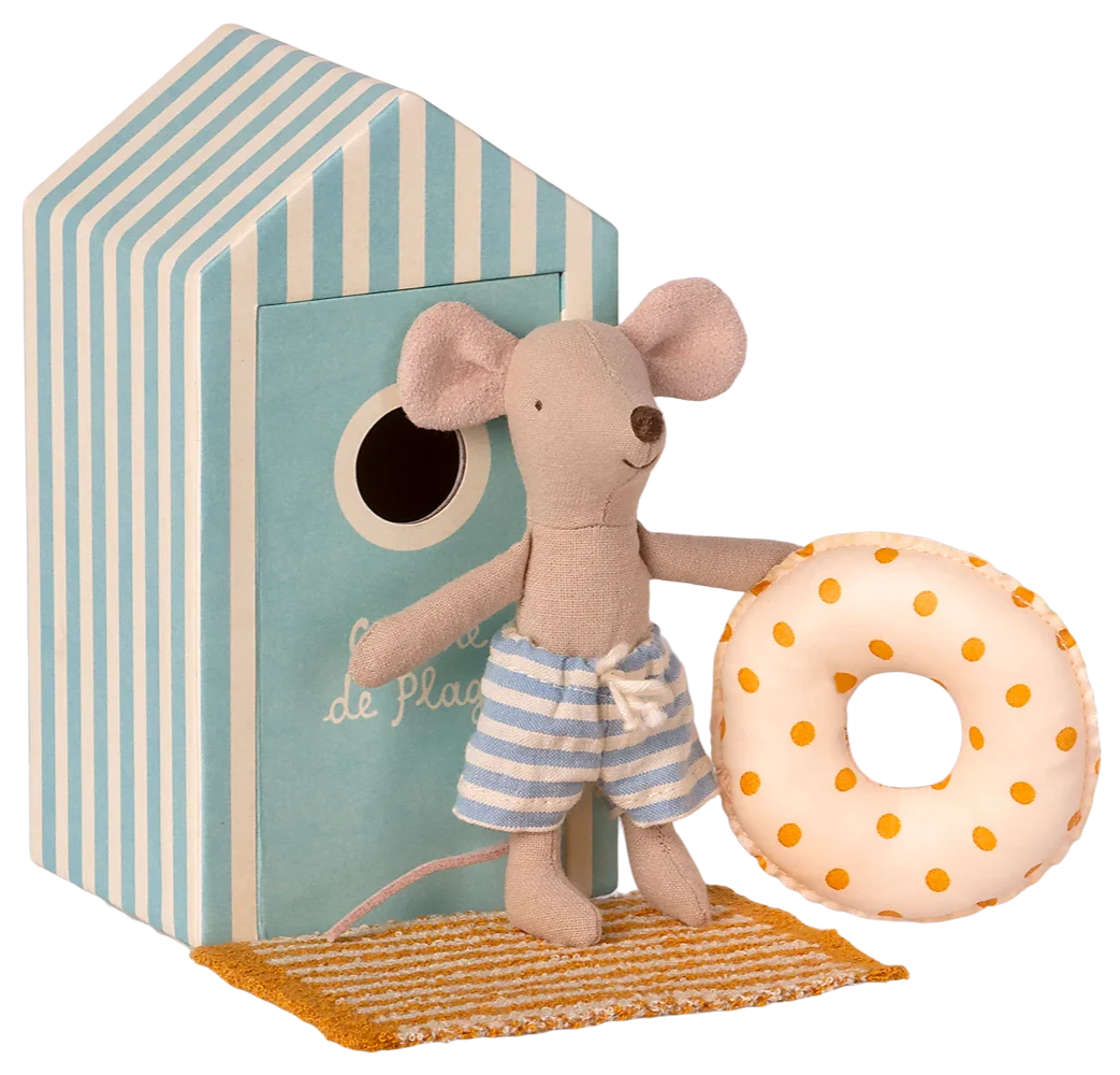 A toy mouse in a beach outfit, holding a float, standing in front of a striped beach house.