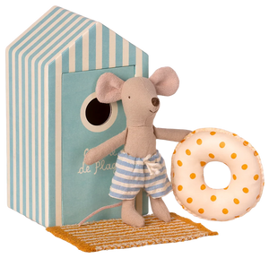 A toy mouse in a beach outfit, holding a float, standing in front of a striped beach house.