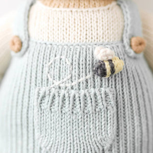The bee detail on the blue overalls of the honey bear stuffed animal. 