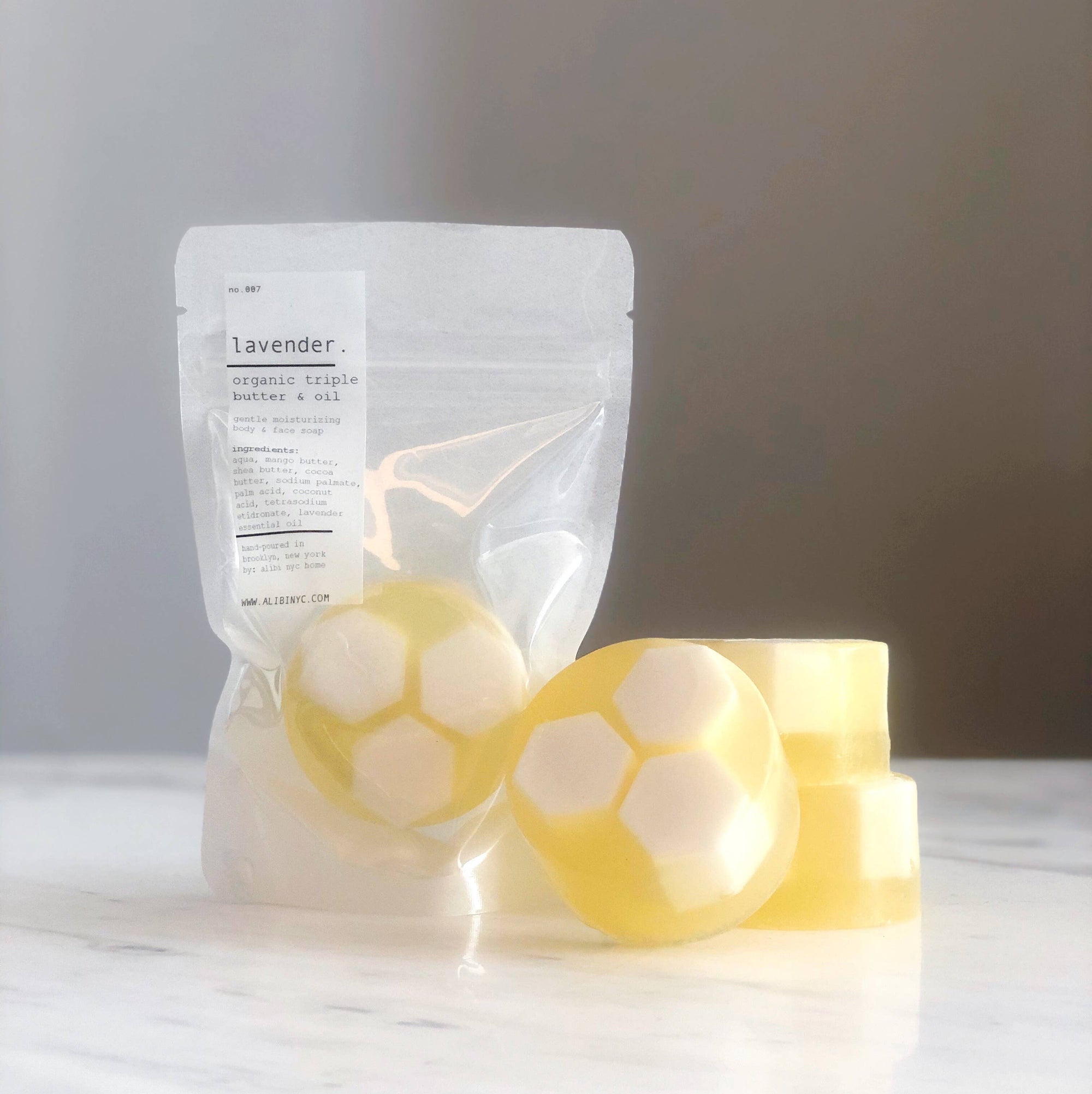Two yellow soap bars with circular designs on a white surface, next to a clear plastic bag labeled 'Lavender'.