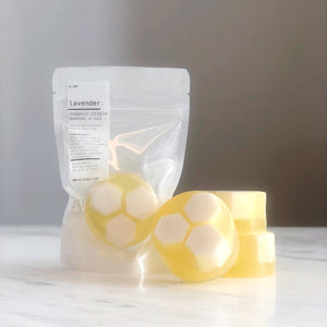 Two yellow soap bars with circular designs on a white surface, next to a clear plastic bag labeled 'Lavender'.
