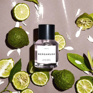 A bottle of Bergamusk perfume, surrounded by limes and greenery. 
