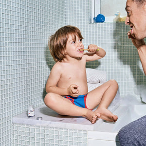 A child and a man brushing their teeth near a bathtub. 