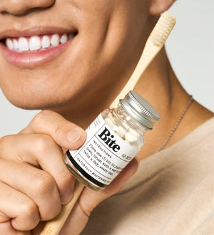 A man holding a bamboo toothbrush and a bottle of toothpaste bits. 