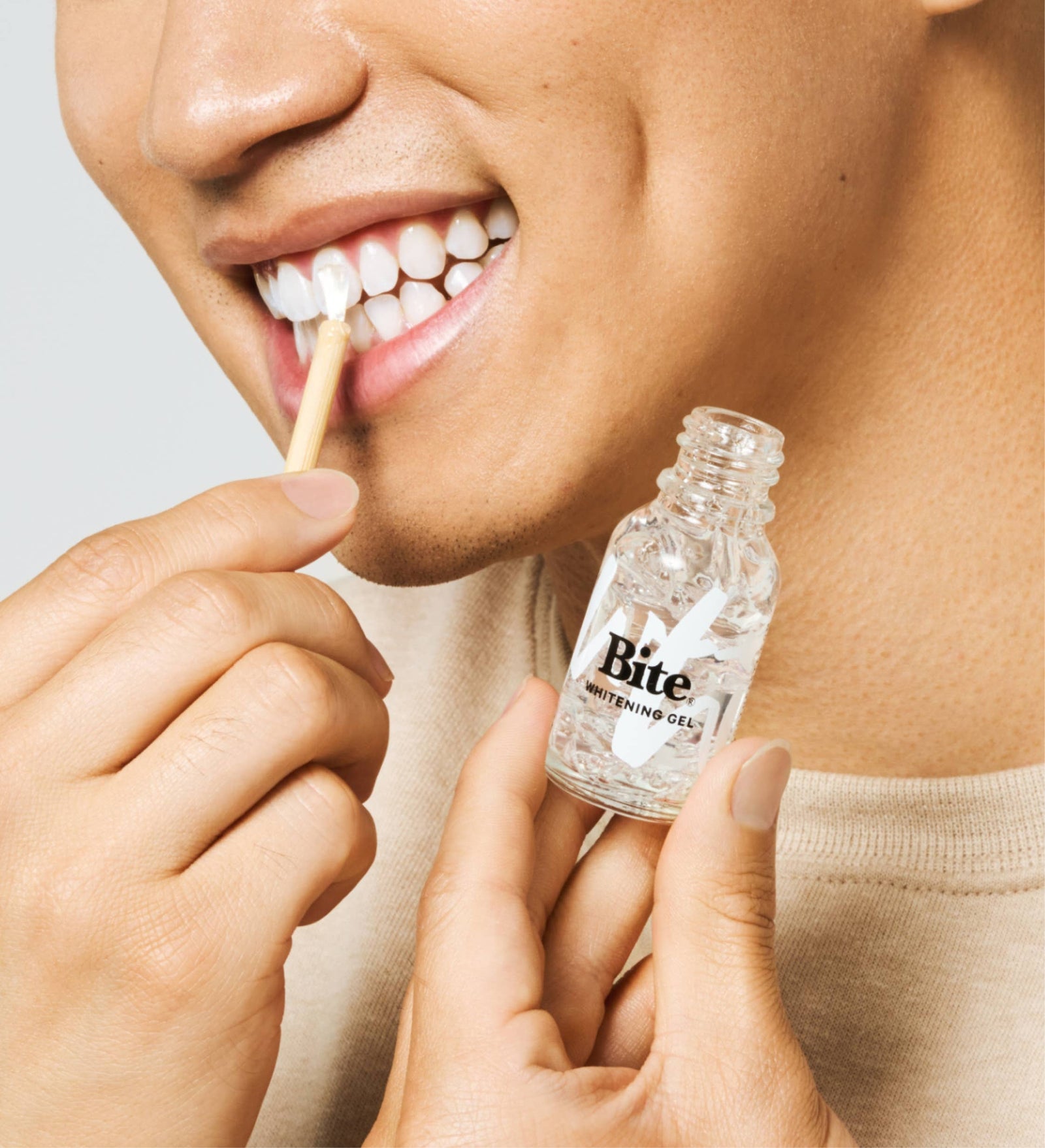 A bottle of Bite Tooth Whitening Gel, next to a bamboo applicator.