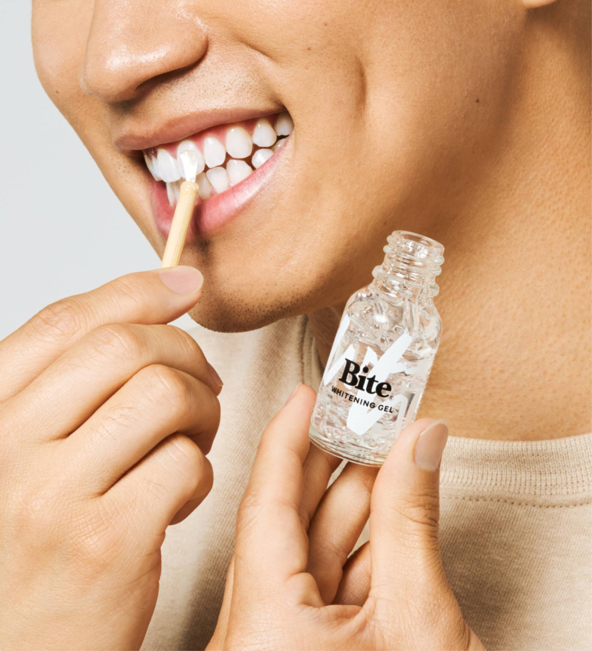 A bottle of Bite Tooth Whitening Gel, next to a bamboo applicator.