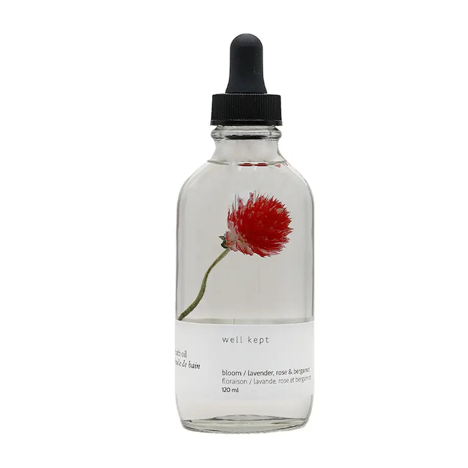A clear glass bottle with a dropper filled with bath oil, featuring a red flower illustration on the label and the brand name 'Well Kept'.