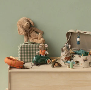 Collection of children's toys including a teddy bear, toy car, and suitcase on a wooden surface with a green wall background.