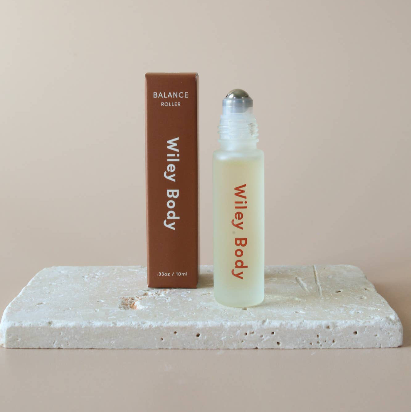 A Wiley Body balance roller oil bottle with a brown label, placed on a white surface against a beige background.