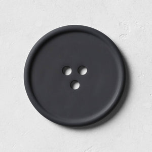 A round black concrete tray with a button-like shape, featuring subtle textures on its surface, designed for holding everyday favorites.