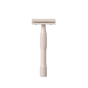 A brass safety razor with a stainless steel blade, cream-colored handle, and textured grip area.