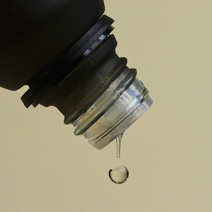 Close-up of a black and clear bottle cap with a droplet on a beige background