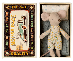 A toy mouse in a matchbox, with the mouse dressed in a pajama set and the matchbox interior featuring a blue and beige design. The matchbox lid has a vintage style with a graphic of a car and the text 'Best Quality'.