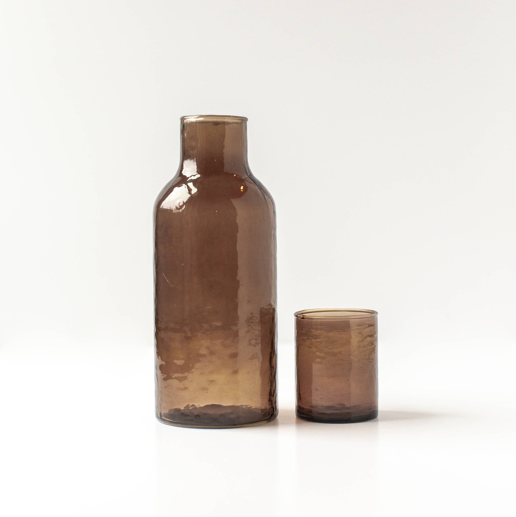 A brown glass decanter next to a brown glass cup that also serves as a lid. 