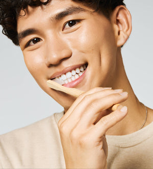 A man with short dark hair with a bamboo toothbrush in his mouth. 