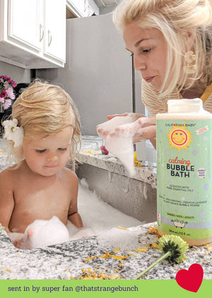 Woman and child in a bathtub with a bottle of Calming Bubble Bath.