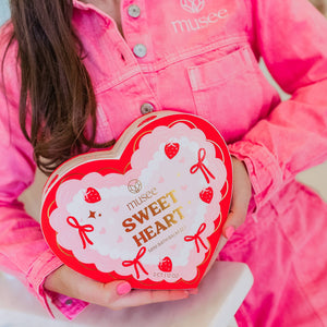 Person wearing a pink jacket holding a heart-shaped 'Musée' product box.