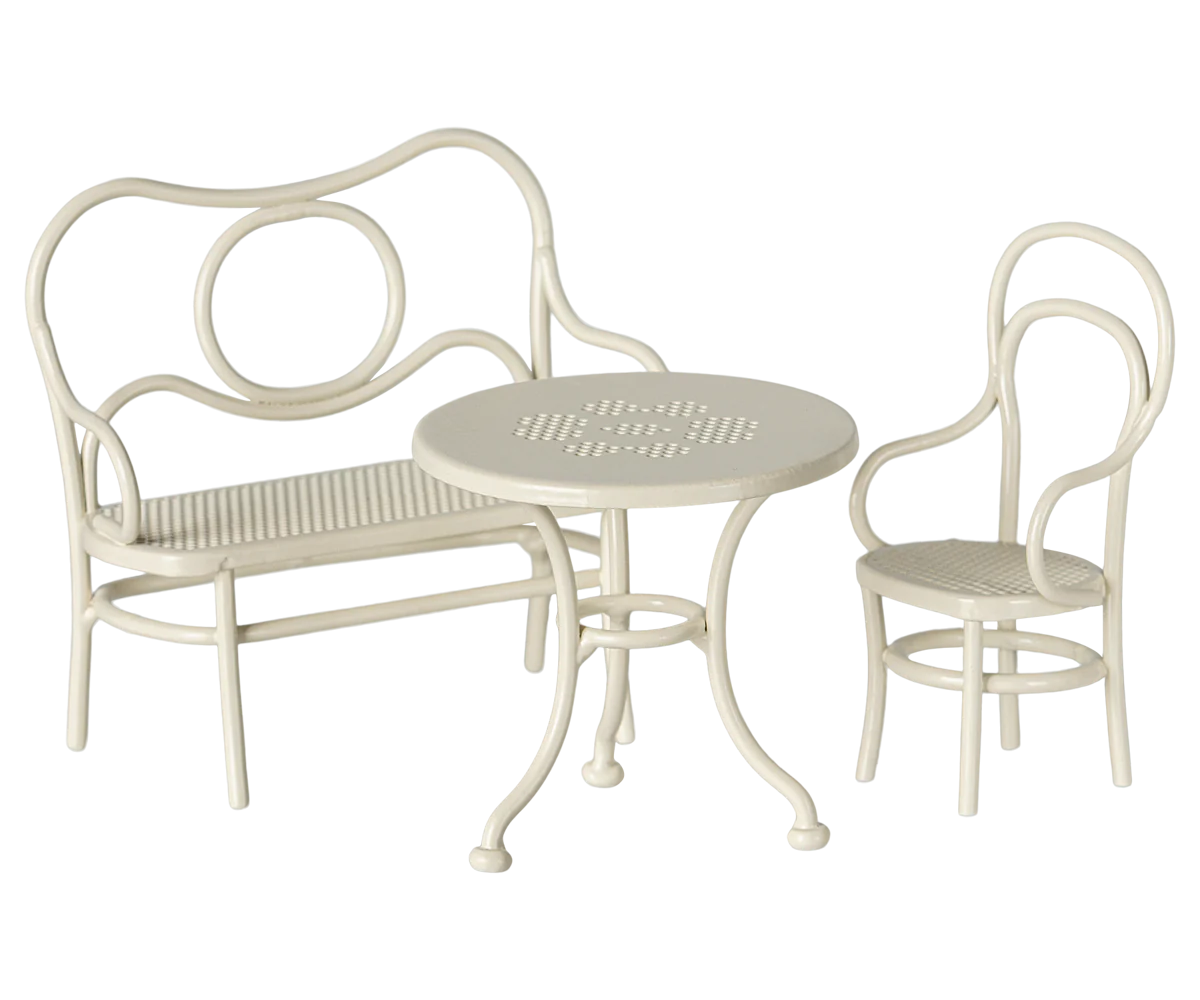 A toy cafe set in off white, consisting of a bench, a chair, and a round table.