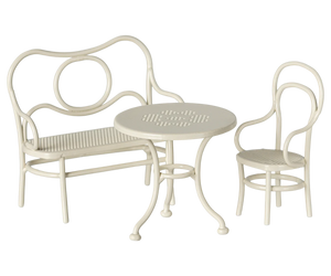 A toy cafe set in off white, consisting of a bench, a chair, and a round table.