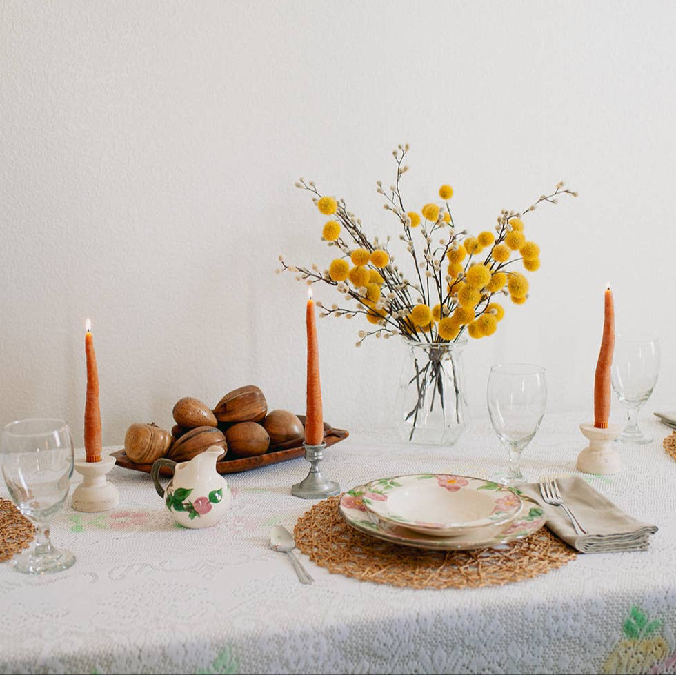 A pair of carrot taper candles, made by Happy Organics in California, on a table with plates and flowers