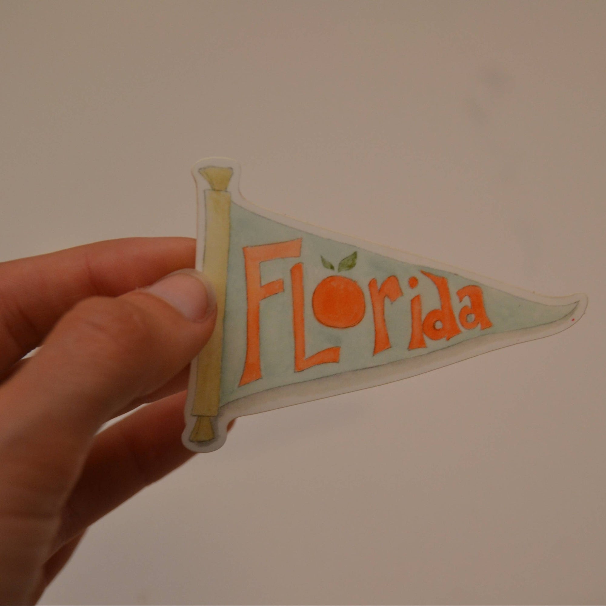 Hand holding a small pennant flag with 'Florida' printed on it against a plain background