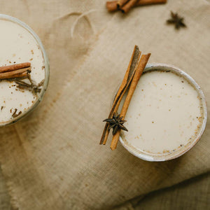 Two ceramic bowls with a creamy substance, garnished with cinnamon sticks and star anise, on a textured fabric background.