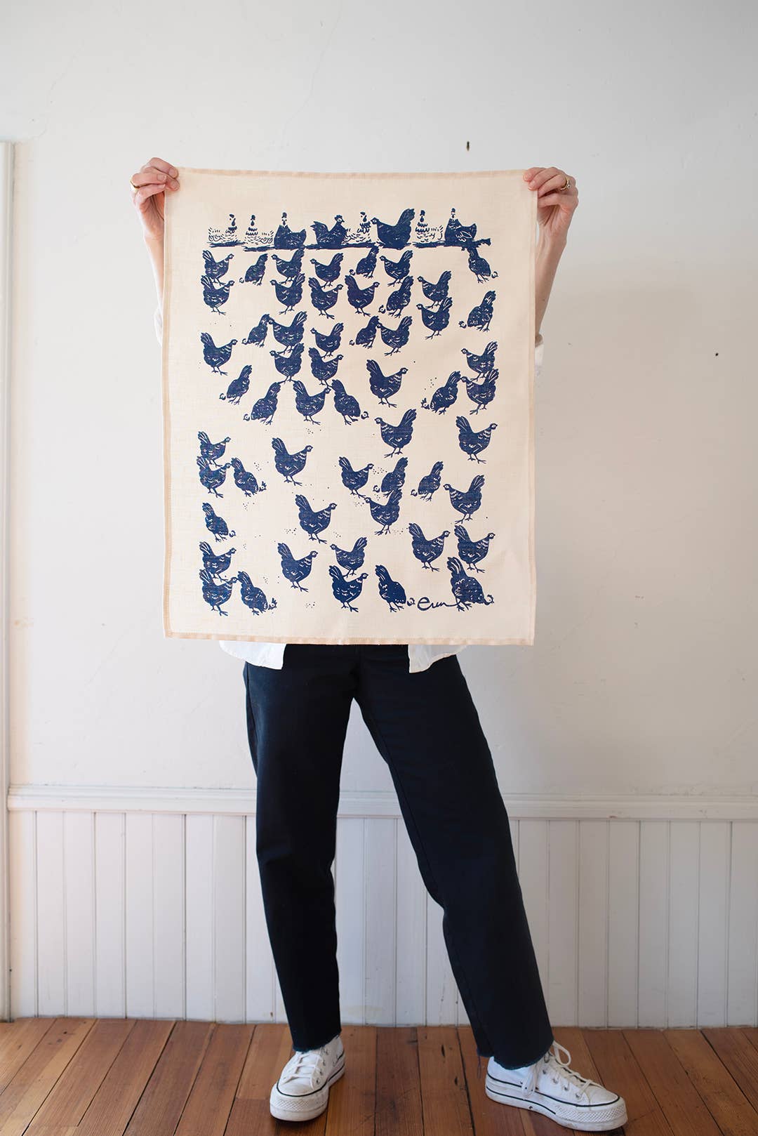 Person holding a tea towel with blue chicken pattern against a white wall.