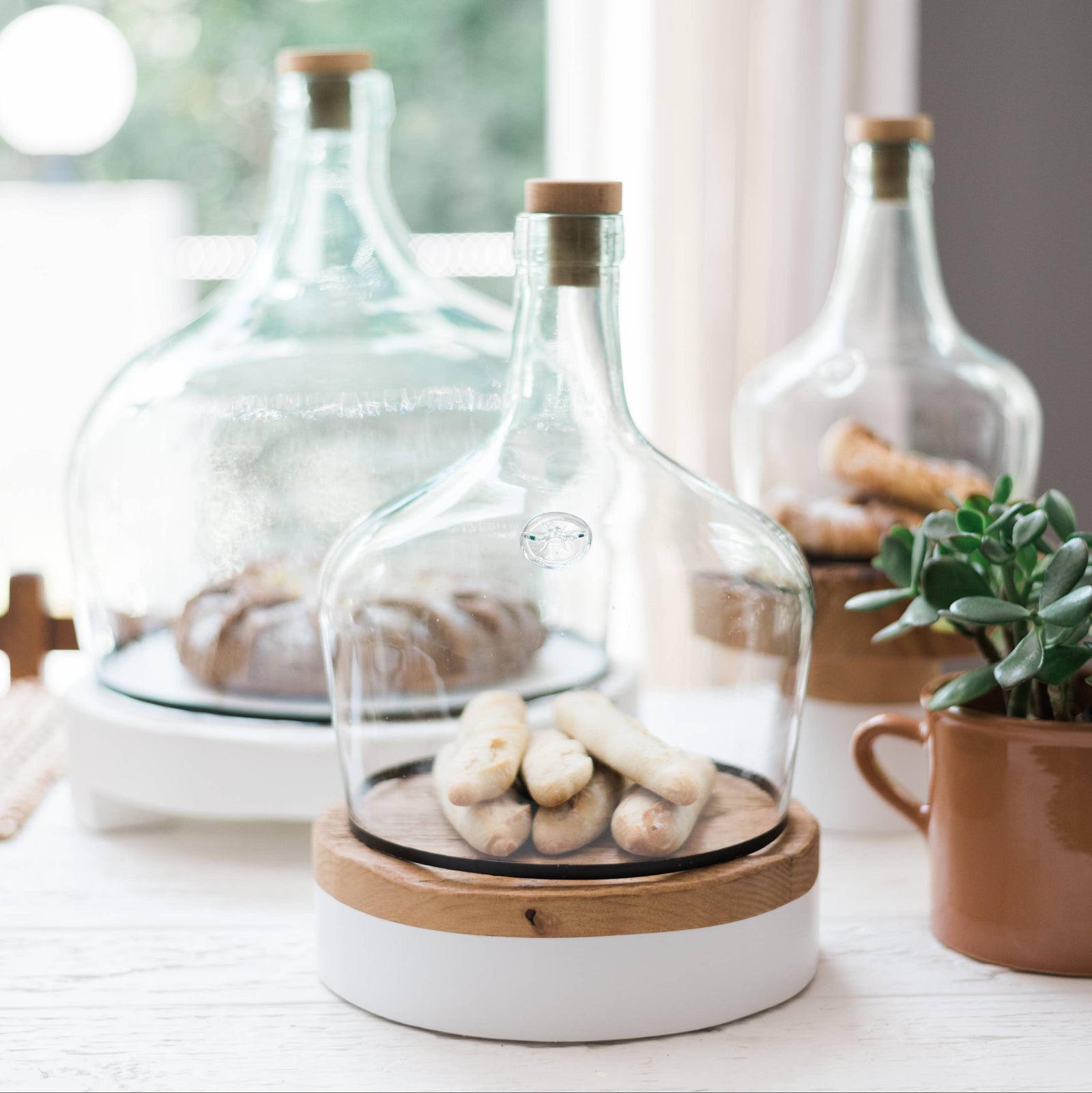 Three glass cloches on a table covering baked goods. 