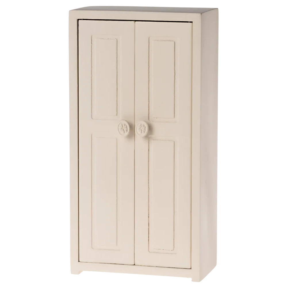 A small toy closet for mice with a cream color, made of wood, featuring two doors and three golden hangers inside.