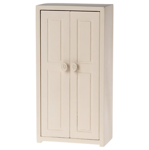 A small toy closet for mice with a cream color, made of wood, featuring two doors and three golden hangers inside.