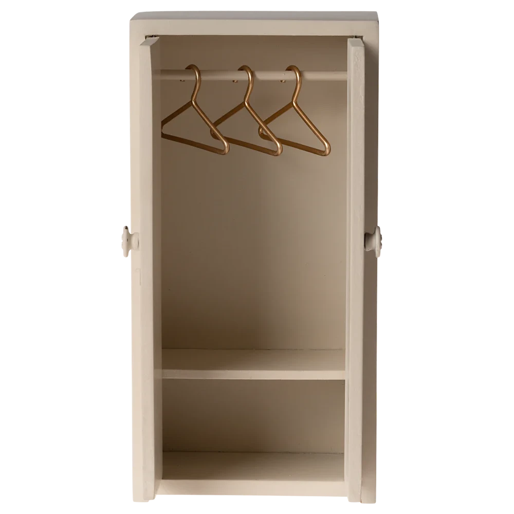 A small toy closet for mice with a cream color, made of wood, featuring two doors and three golden hangers inside.