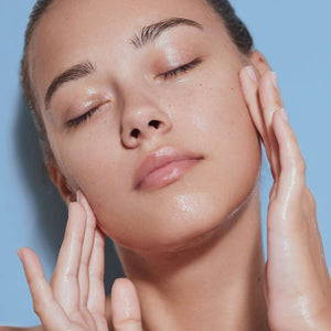 Close-up of a person with hands on their face against a light blue background