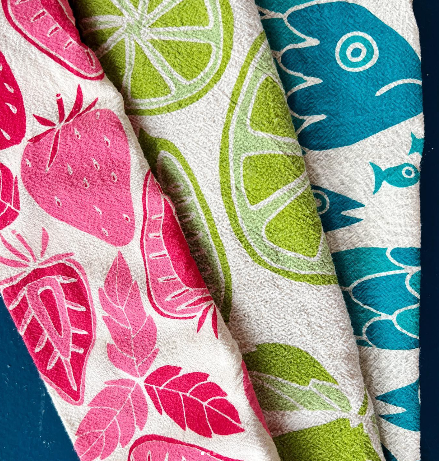 Three colorful tea towels on a dark blue background. 