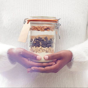 A woman carrying a le parfait glass container with cookie ingredients inside of it. 