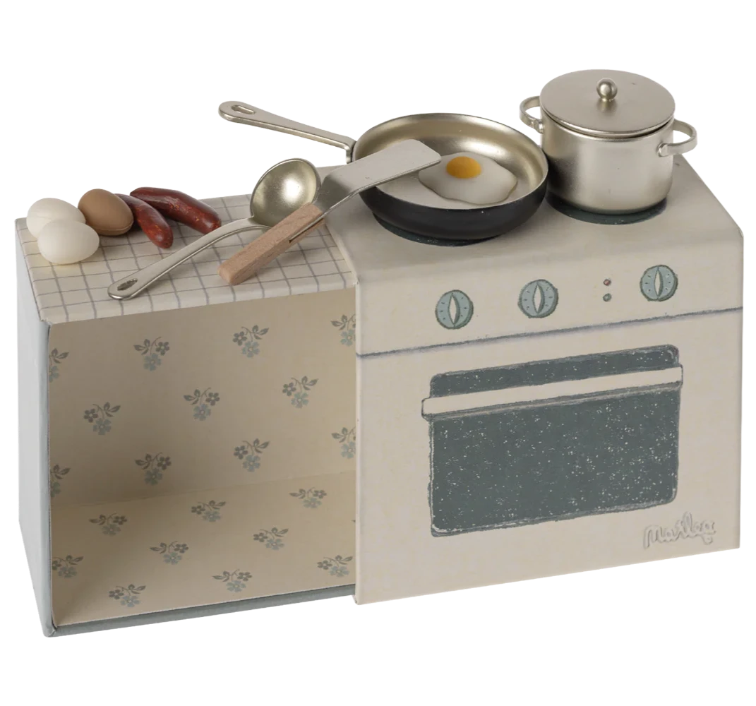 A small, toy kitchen set designed to look like a stove and oven with pretend food items and kitchen utensils on top, all packaged in a box with a floral pattern.