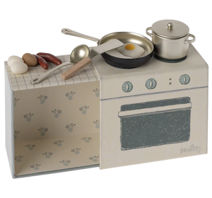 A small, toy kitchen set designed to look like a stove and oven with pretend food items and kitchen utensils on top, all packaged in a box with a floral pattern.