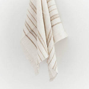 A white cotton tea towel with striped detailing, handwoven in Ethiopia, hanging on a white wall.