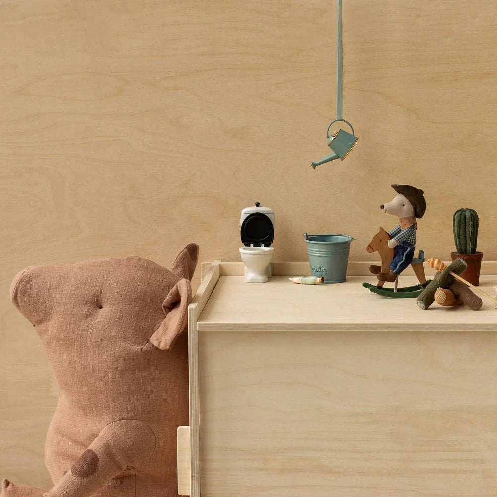 A plush toy mouse dressed as a cowboy, with a blue bandana, brown hat, and blue jeans, riding a small wooden rocking horse.