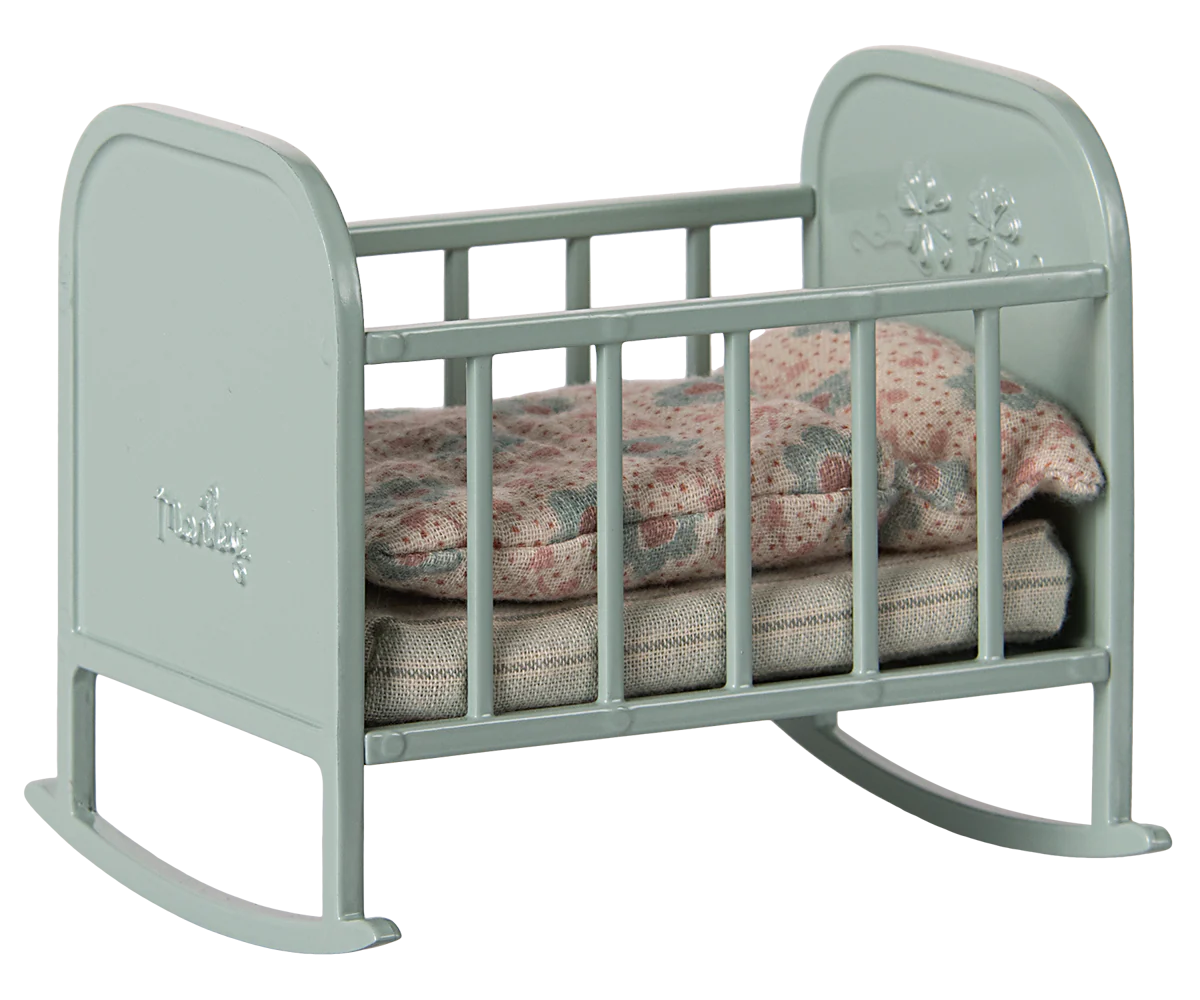 A blue mint colored metal cradle with a soft sleeping bag inside, featuring small flower embossment on the headboard and rounded legs.